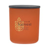 Orange candle with black lid labeled 'harvest pumpkin spice' on an orange background